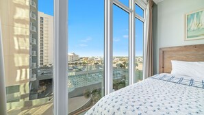 A hotel room with a large window, a bed with a patterned bedspread, and a view of a parking area and buildings. - 3rd Floor!! New Owner, Zero Entry Pool w/ Slide!! (Gulf Shores)