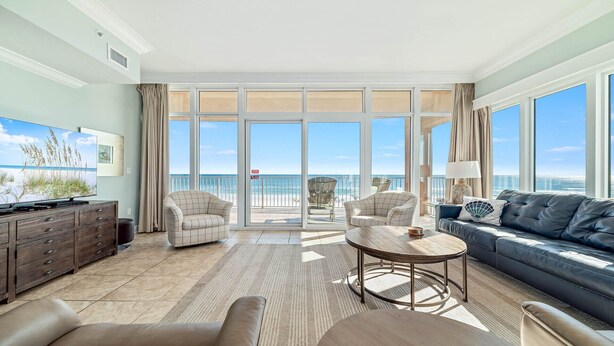 A spacious living room with a large window overlooking the beach, a sofa, two armchairs, a coffee table, and a TV on a wooden cabinet. - 3rd Floor!! New Owner, Zero Entry Pool w/ Slide!! (Gulf Shores)
