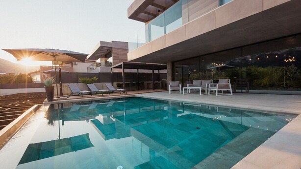 Un área de piscina moderna al aire libre con sillones de descanso y una zona de estar cubierta.