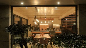 Un comedor moderno con una mesa grande, sillas, lámparas colgantes y una cocina al fondo.