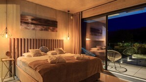 Un dormitorio moderno con una cama grande, dos lámparas de noche, vistas al exterior y un balcón con sillas.