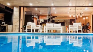 Un área de piscina interior moderna con sillones blancos y una piscina azul cristalina.