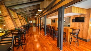 Un'area pranzo lunga e stretta con pavimento in legno e sedie in metallo nero. Sono presenti diversi tavoli e una zona bar con sgabelli.