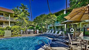 A pool area with lounge chairs and umbrellas, surrounded by a fence and palm trees. - Nautical Theme Garden View Studio - Kona Islander Inn Condos Condo by RedAwning (Kailua-Kona)