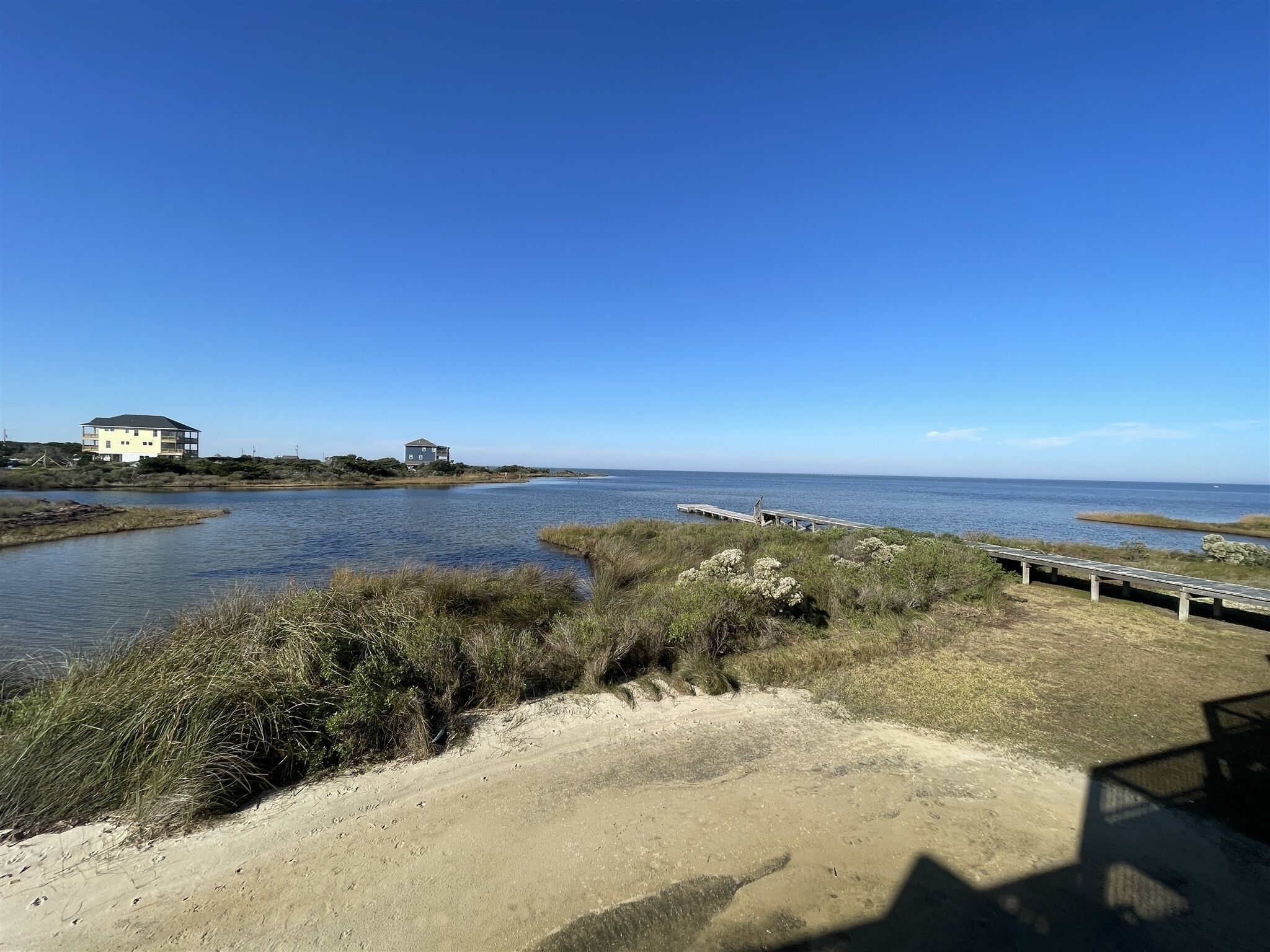 A coastal landscape with a sandy beach, a wooden pier, and two buildings near the water.