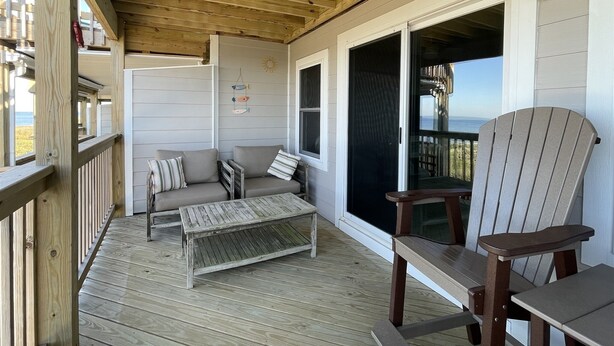 A covered deck with a wooden ceiling, a sofa, a table, and a chair. - Sw 3 Finns Up 1 Bedroom Condo by RedAwning (Hatteras)