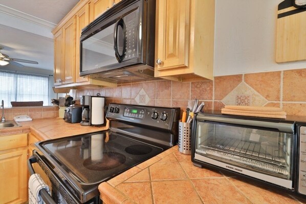 A kitchen with wooden cabinets, a black microwave, a stove, and a toaster oven.