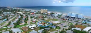 An aerial view of a coastal town with a beachfront hotel, surrounded by residential buildings and a marina.