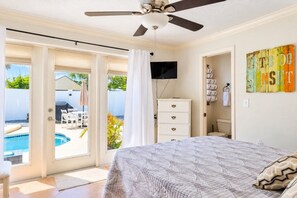 Un dormitorio con cama, ventilador de techo, televisor y vistas a una piscina.