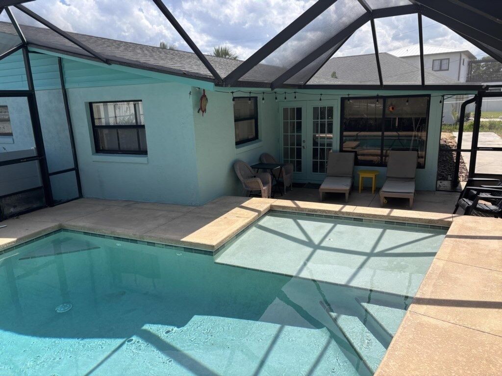 A covered pool area with a patio, chairs, and a small table.