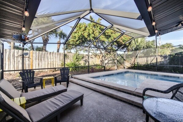 Relax by the pool surrounded by lush trees and a clear sky.