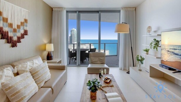 A modern hotel room with a balcony, a sofa, a coffee table, and a TV. - Oceanfront Elegance: Sunset Views, Pet-Friendly (Hollywood)