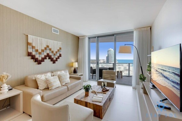 A modern hotel room with a large window offering a city view, a flat-screen TV, a wooden coffee table, and a sofa. - Oceanfront Elegance: Sunset Views, Pet-Friendly (Hollywood)