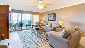 A living room with a ceiling fan, a sofa, a coffee table, and a view of the balcony. - Recently Renovated Beach Condo with Large Patio Deck and Ocean View by RedAwning (Fernandina Beach)