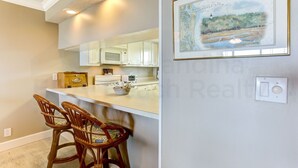 A kitchen with white cabinets, a microwave, and a painting of a coastal scene. - Recently Renovated Beach Condo with Large Patio Deck and Ocean View by RedAwning (Fernandina Beach)
