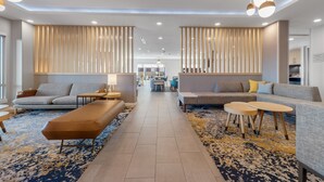 Eine moderne Hotelhalle mit einer zentralen Sitzecke, einem Empfangsbereich und Blick in den Speisesaal.