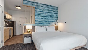Ein Hotelzimmer mit Bett, Nachttisch, Lampe und Blick auf die Küche.