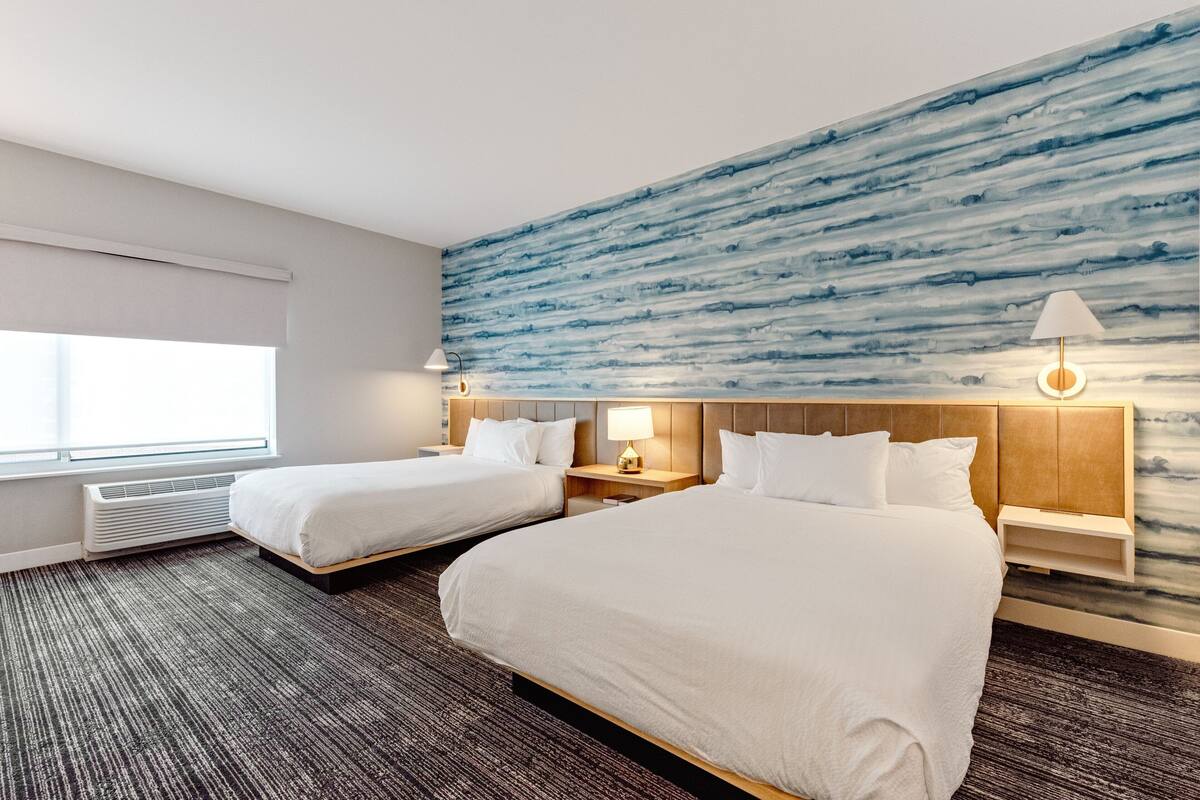 Habitació d'hotel amb dos llits, un finestral gran, un mural a la paret i un disseny modern.
