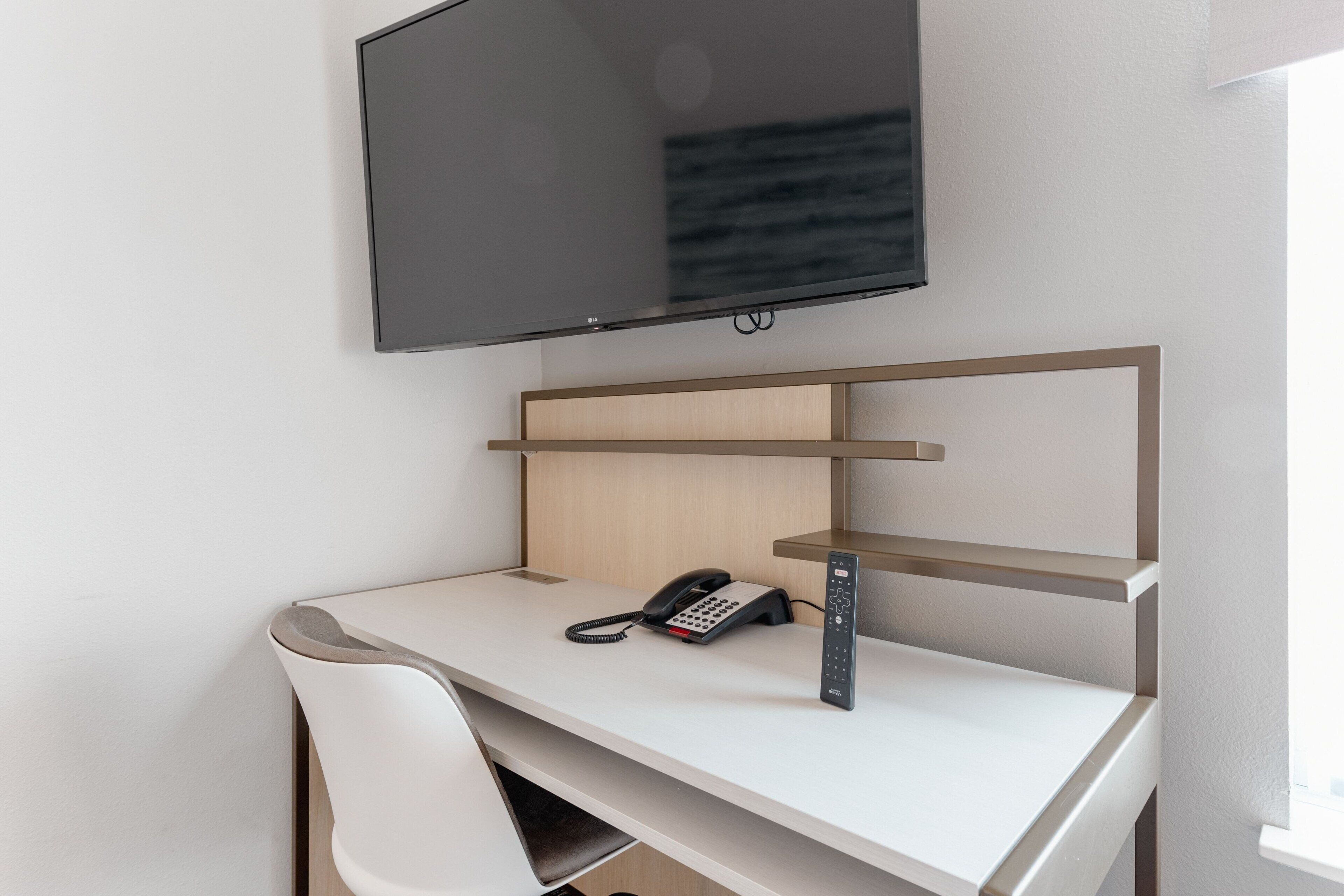 A modern office desk with a telephone, a mounted television, and a shelf.