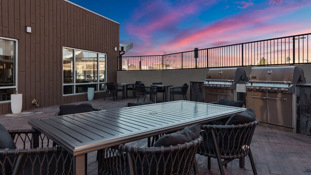 Eine Außenpatio mit Holztisch und -stühlen, einem Grill und Blick auf den Sonnenuntergang.