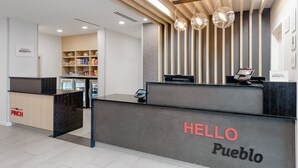 Ein Hotelrezeptionstresen mit einem 'HELLO Pueblo'-Schild, einem 'Marriott Bonvoy'-Schild und einem 'PINCH'-Schild.