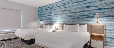 A hotel room with two beds, a large window, a wall with a blue abstract design, and a nightstand with a lamp.