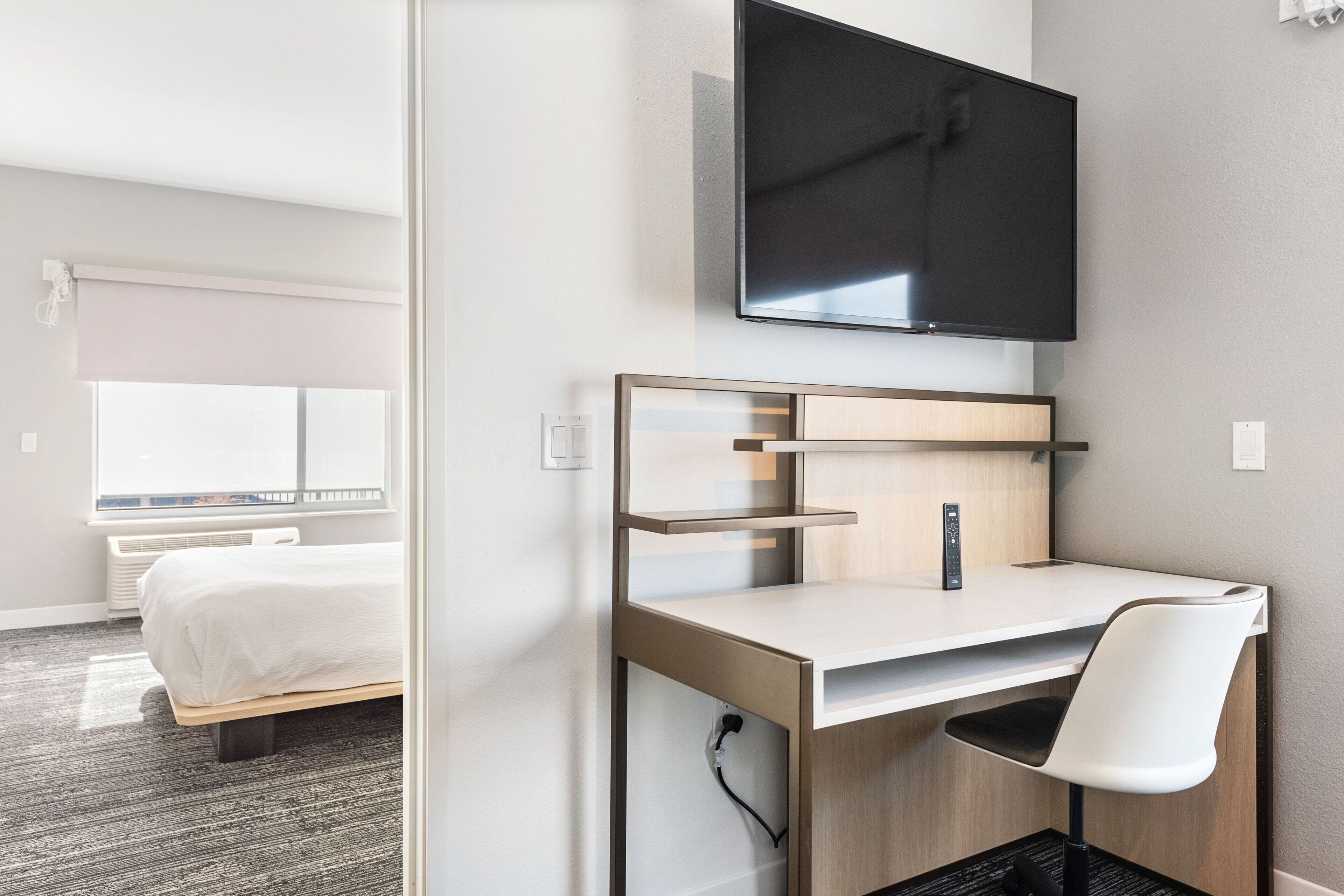 Ein Hotelzimmer mit Bett, Schreibtisch mit Stuhl, Flachbildfernseher und Fenster mit Jalousien.
