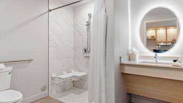A modern bathroom with a glass-enclosed shower, a white toilet, a sink with a mirror, and a wooden vanity.