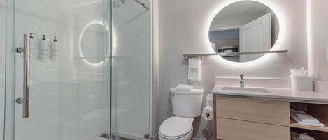A modern bathroom with a glass-enclosed shower, a toilet, a sink with a mirror, and neatly folded towels.