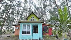 Una casita pequeña y colorida con techo verde y puerta azul, rodeada de árboles.