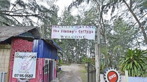 A rustic cottage entrance with a sign reading "Selamat Datang The Sibling's Cottage Welcome" and a contact number.