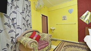 A room with a sofa, a patterned rug, a wall-mounted sink, and a fan.