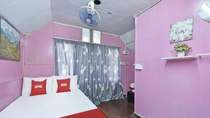 A bedroom with a bed, a ceiling fan, a window with curtains, a wall-mounted shelf with a plant, and a painting on the wall.