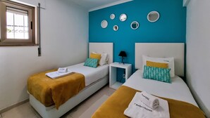 Habitació d'hotel amb dos llits, una finestra, una paret d'accent blau i una petita taula de nit amb una làmpada.