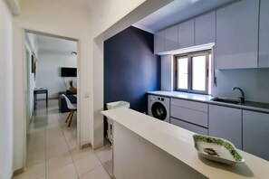 A modern kitchen with grey cabinets, a washing machine, and a window above the sink.