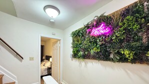 A hallway with a staircase, a neon sign, and a wall-mounted plant display. - Entire Unit-5min to M&TBank Camden Yards (Baltimore)