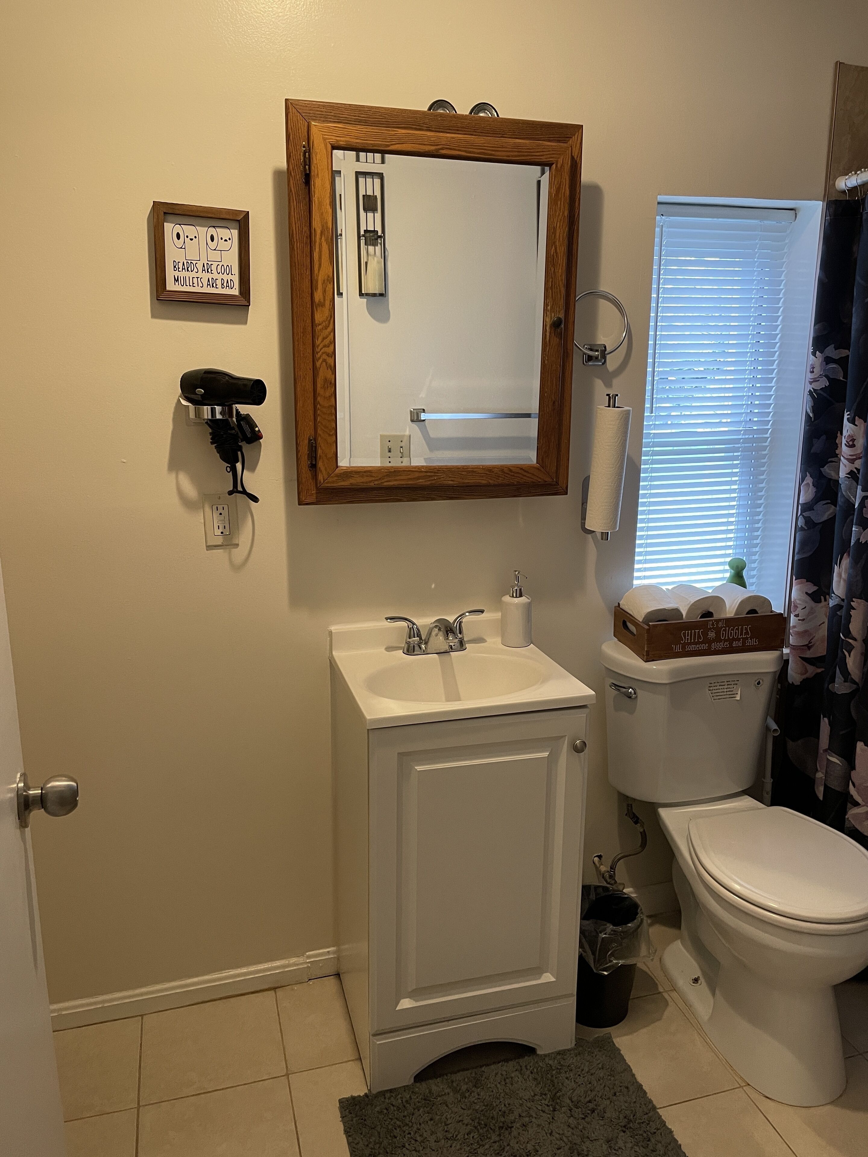 A bathroom with a wooden-framed mirror, a white sink with a faucet, a toilet, and a shower curtain.
