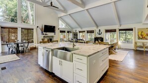Een ruime keuken met een groot kookeiland, houten vloeren en een hoog plafond met zichtbare balken.