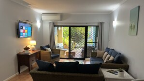 Uma sala de estar com televisão, sofá, mesa de centro e espaço para refeições.