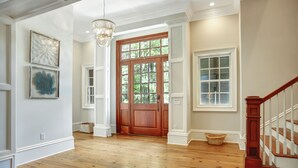 Un pasillo amplio con suelo de madera, una puerta de madera y una escalera con barandilla de madera.