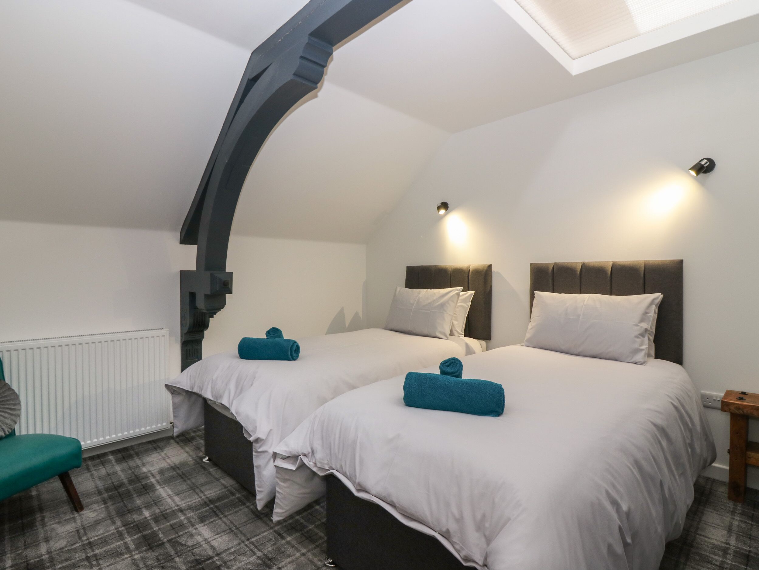A bedroom with two beds, a window, a radiator, and a small table.