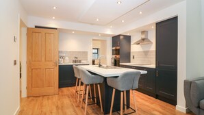 A modern kitchen with a central island, bar stools, and a built-in oven. - The Reception Room at The Institute Executive Apartments (Keith)