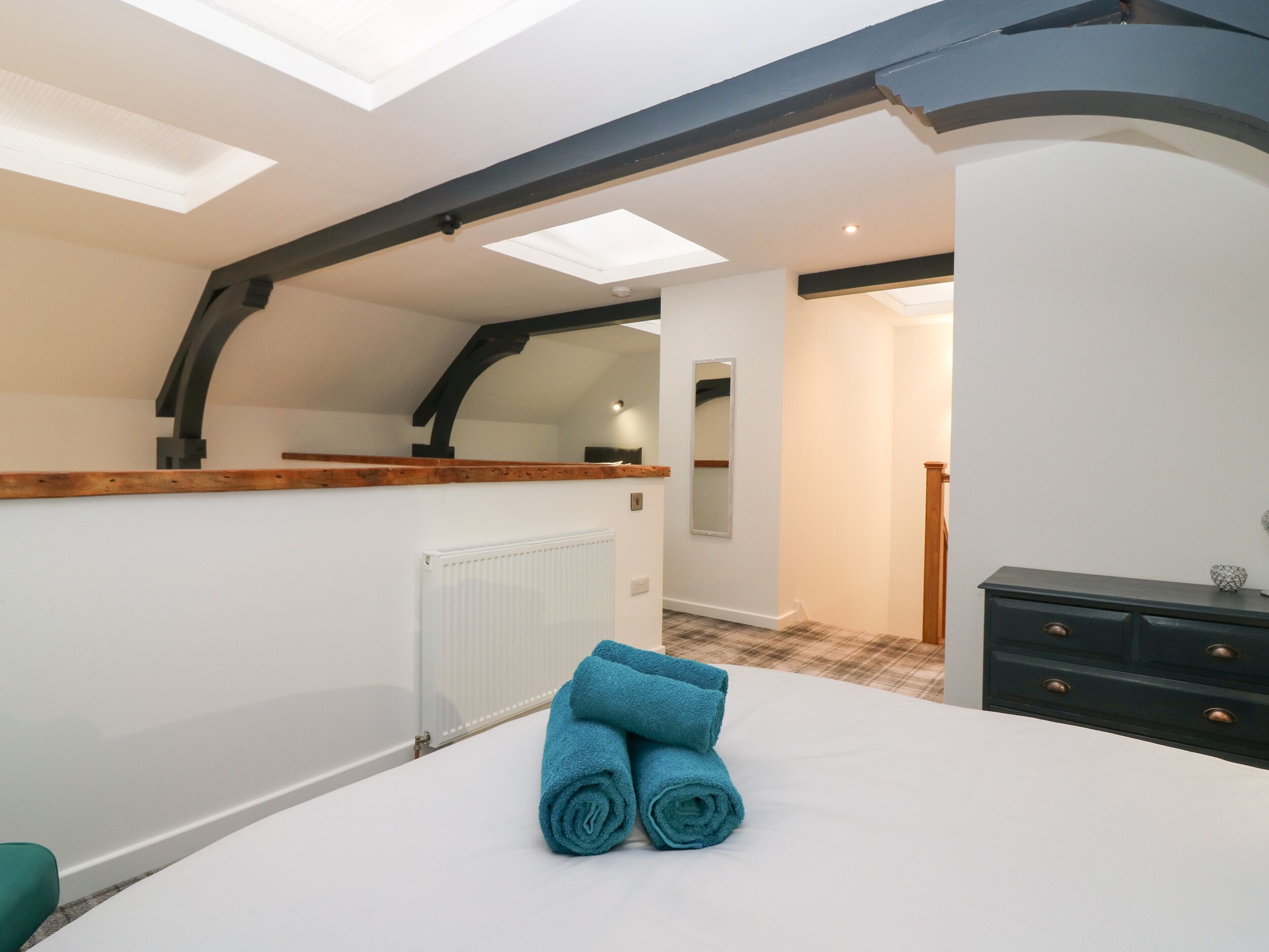 A bedroom with skylights, a wooden ceiling, a radiator, a bed with blue towels, a dresser, and a mirror.