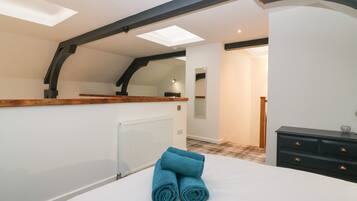 A bedroom with skylights, a wooden ceiling, a radiator, a bed with blue towels, a dresser, and a mirror.