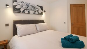 A bedroom with a large bed, a headboard, a wall-mounted light, a door, and a painting. - The Reception Room at The Institute Executive Apartments (Keith)