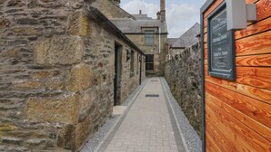 A narrow stone corridor with a wooden wall on one side and a stone building on the other. A sign indicates directions to the reception room and the marriage room. - The Reception Room at The Institute Executive Apartments (Keith)