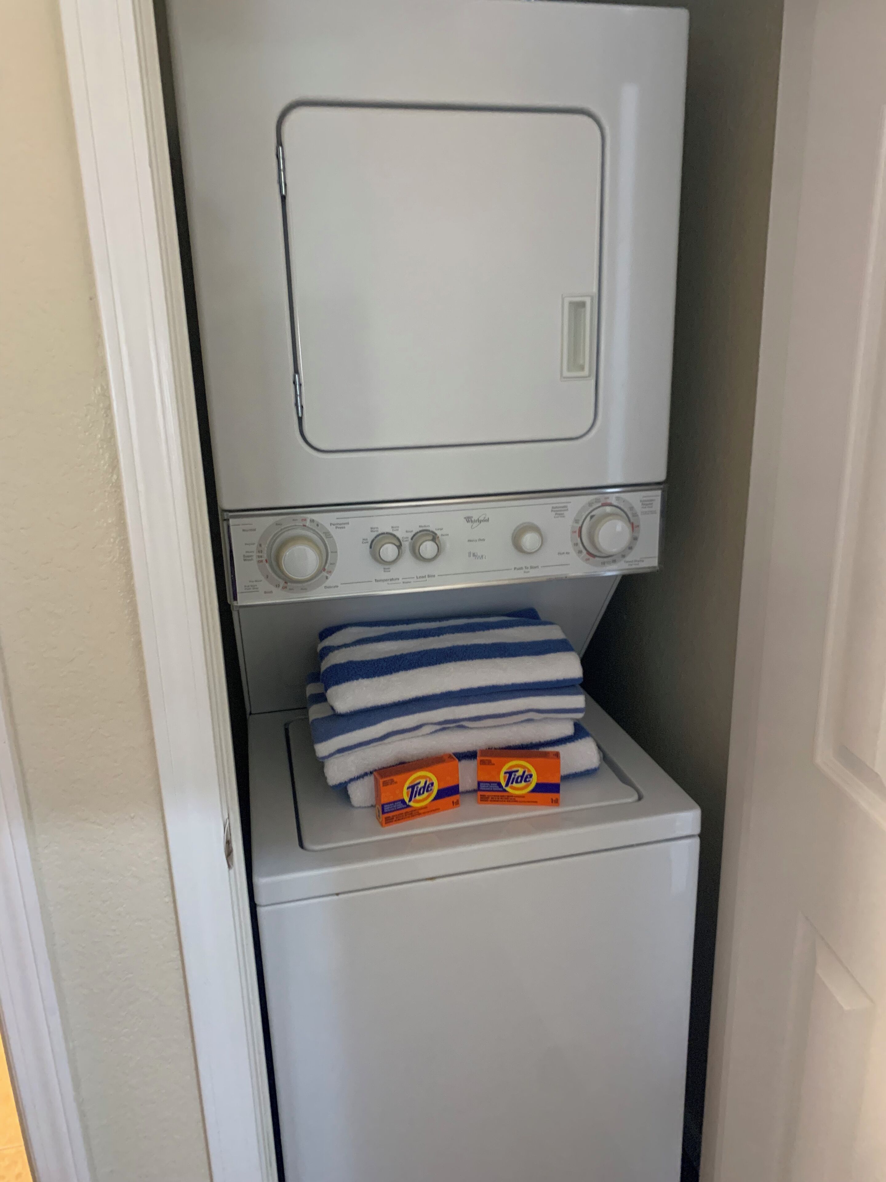 A compact, white laundry machine with a front-loading door, stacked blue and white striped towels, and two Tide detergent boxes.