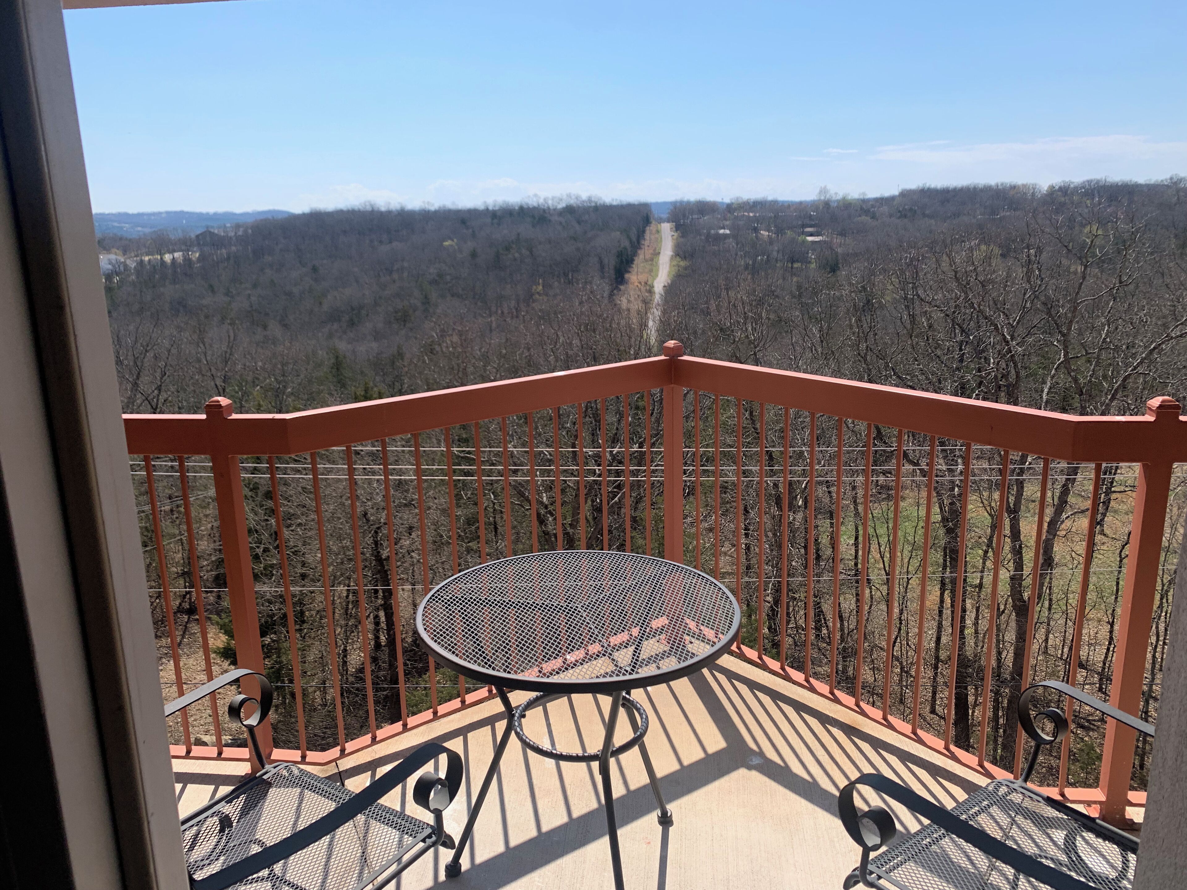 Ein Balkon mit einem Metalltisch und Stühlen, der einen Blick auf eine bewaldete Landschaft bietet.