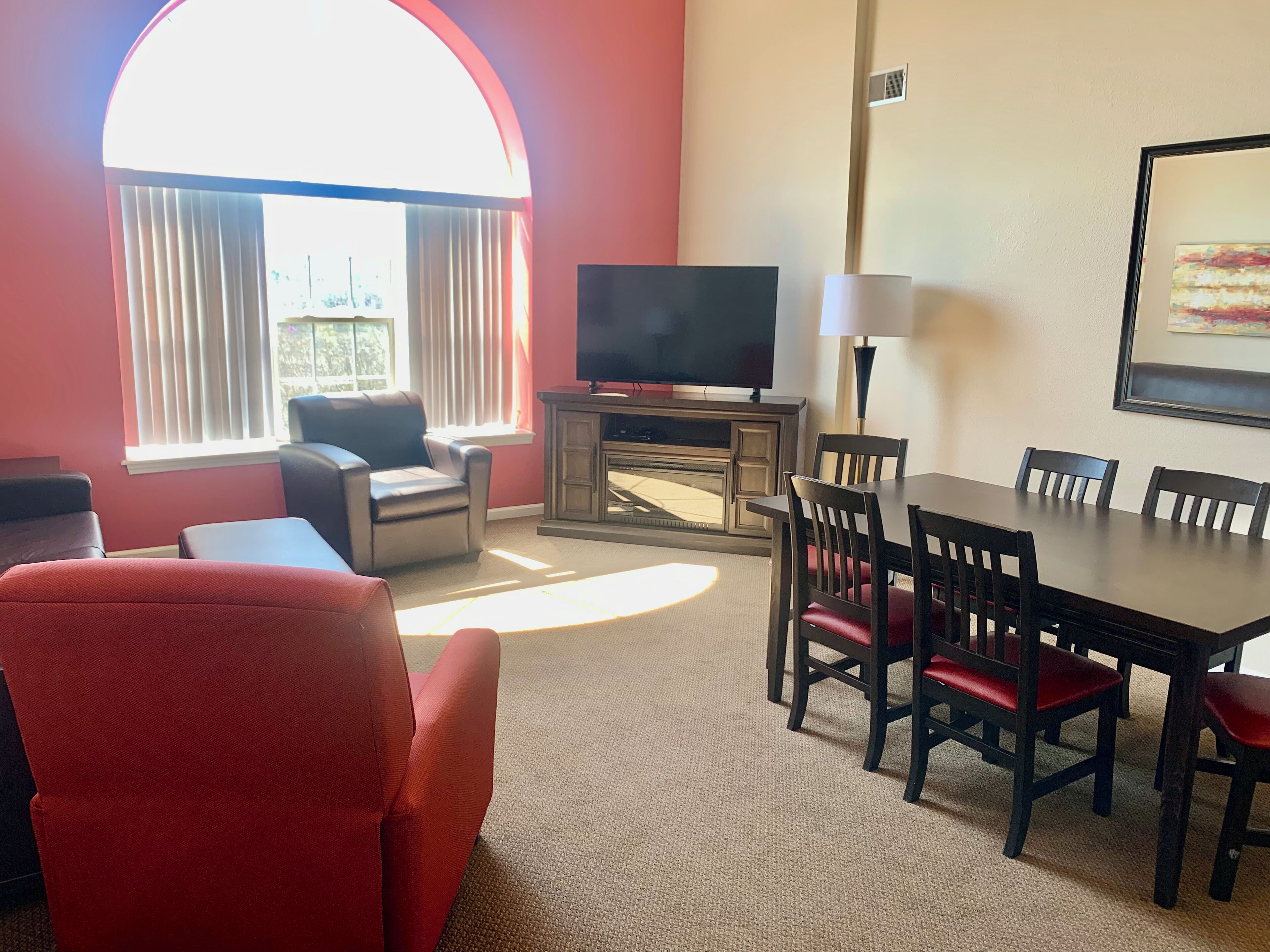 A living room with a TV, a dining table, and red chairs.
