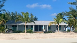 A beachfront property with a large house, palm trees, and clear blue water.